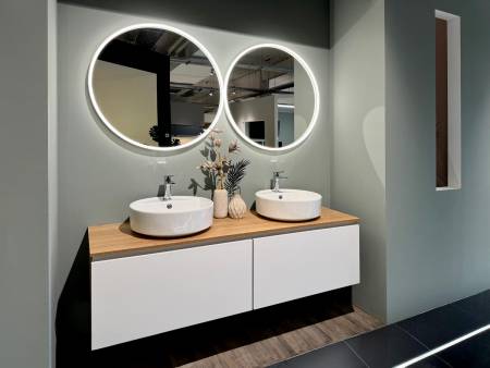 Moderne Badezimmereinrichtung mit zwei kreisförmigen Spiegeln und Doppelwaschbecken auf einem Holzunterschrank.
