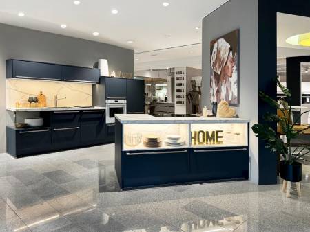 Moderne Küche in Dunkelblau mit goldfarbenen Akzenten, Marmor-Rückwand und "HOME"-Schriftzug im Regal.