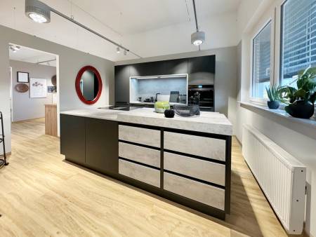 Moderne Kücheneinrichtung mit schlichter schwarzer Kochinsel, grauen Arbeitsplatten und Holzboden, mit stilvollen Hängelampen und einem roten, runden Spiegel an der Wand.