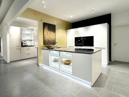 Heller und luftiger Küchenraum mit einer zentralen weißen Insel, hinterleuchteten Glasschränken und einem auffälligen goldenen Gemälde vor einer gelben Akzentwand.