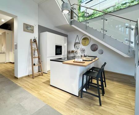 Moderne Küche mit weißer Insel und schwarzen Barhockern, neben einer Glastreppe, mit Holzfußboden und dekorativen Wandplatten.